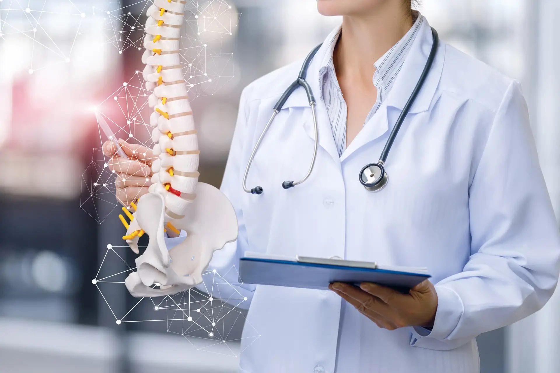 Orthopedist with stethoscope around her neck, clipboard in her left hand, and a 3-D rendering of a spine