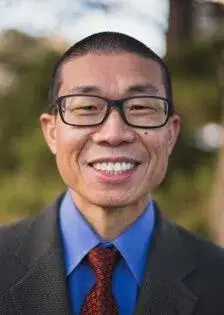 Orthopedist Dr. Manny Moy with a warm smile in a suit and tie with rectangular glasses