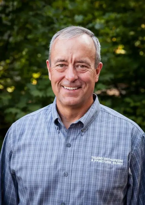 Orthopedist Dr. Ron Bowman smiling in a blue patterned button up shirt